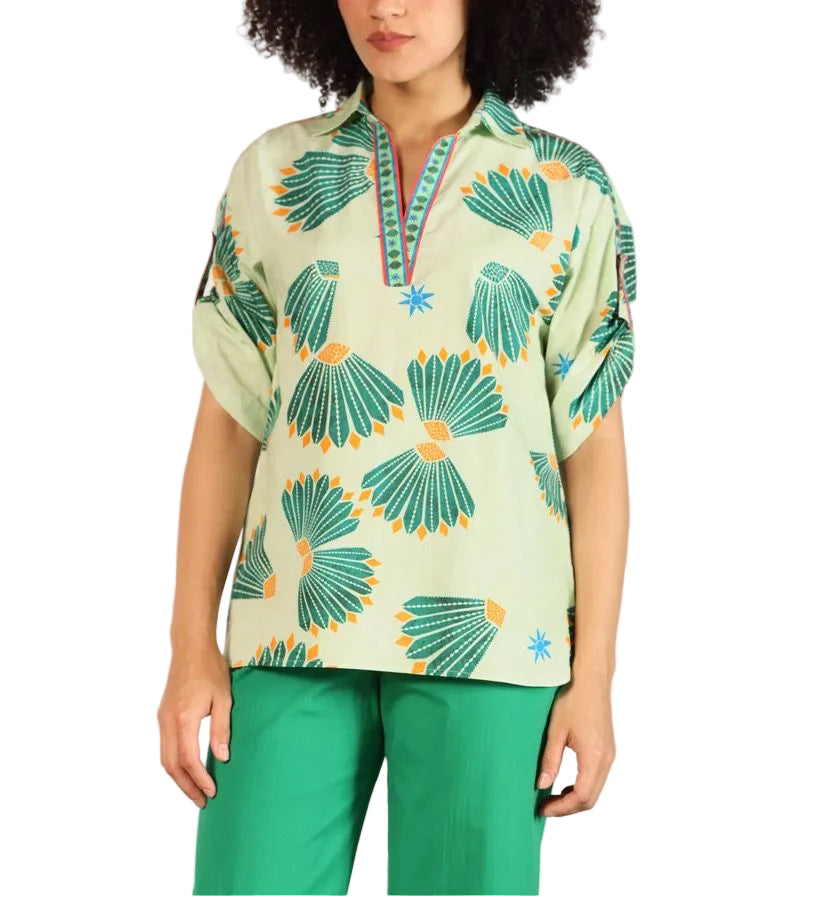 Woman wearing a green patterned blouse and green pants against a beige background