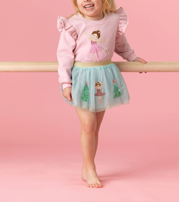 Young girl in a pink sweater and green skirt standing on a pink background