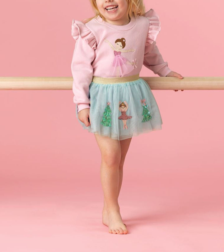 Young girl in a pink sweater and green skirt standing on a pink background