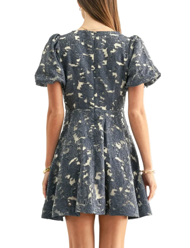 This playful yet refined mini dress brings a rich, tactile element to warm-weather dressing. Crafted from a structured jacquard fabric in a striking denim-blue colorway, the dress features an all-over floral rose pattern woven over a contrasting light backing, making the texture pop. A defined waistline flows effortlessly into a flirty, flared A-line mini dress.