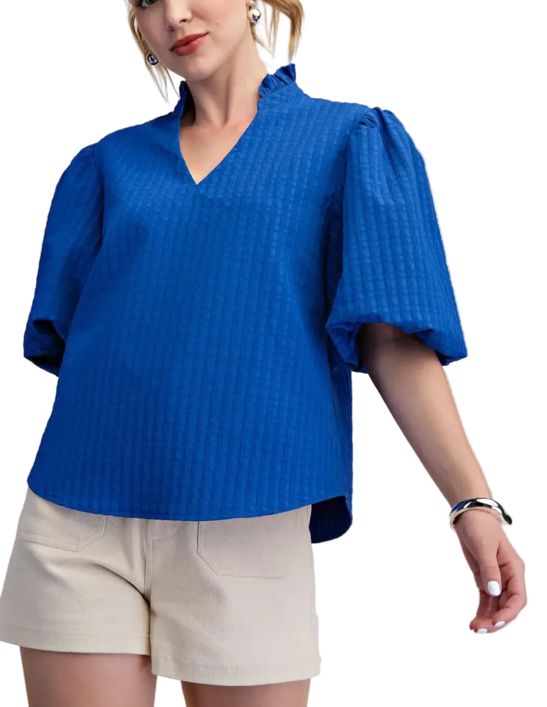 Woman wearing a blue textured blouse and beige shorts on a plain background