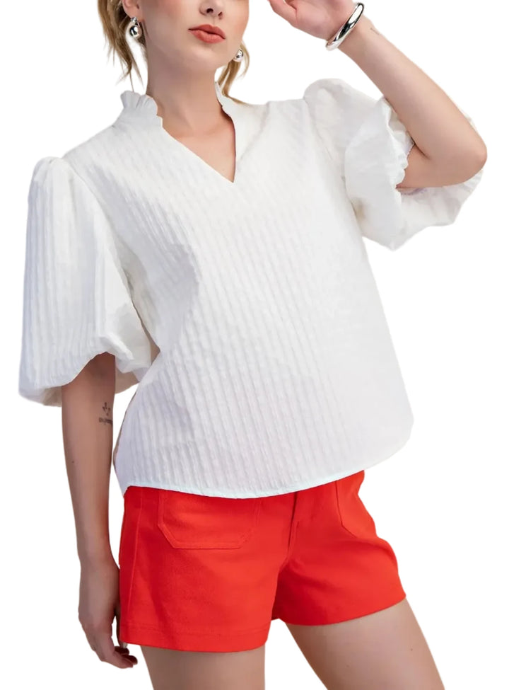 Woman wearing a white blouse with ruffled sleeves and red shorts on a beige background