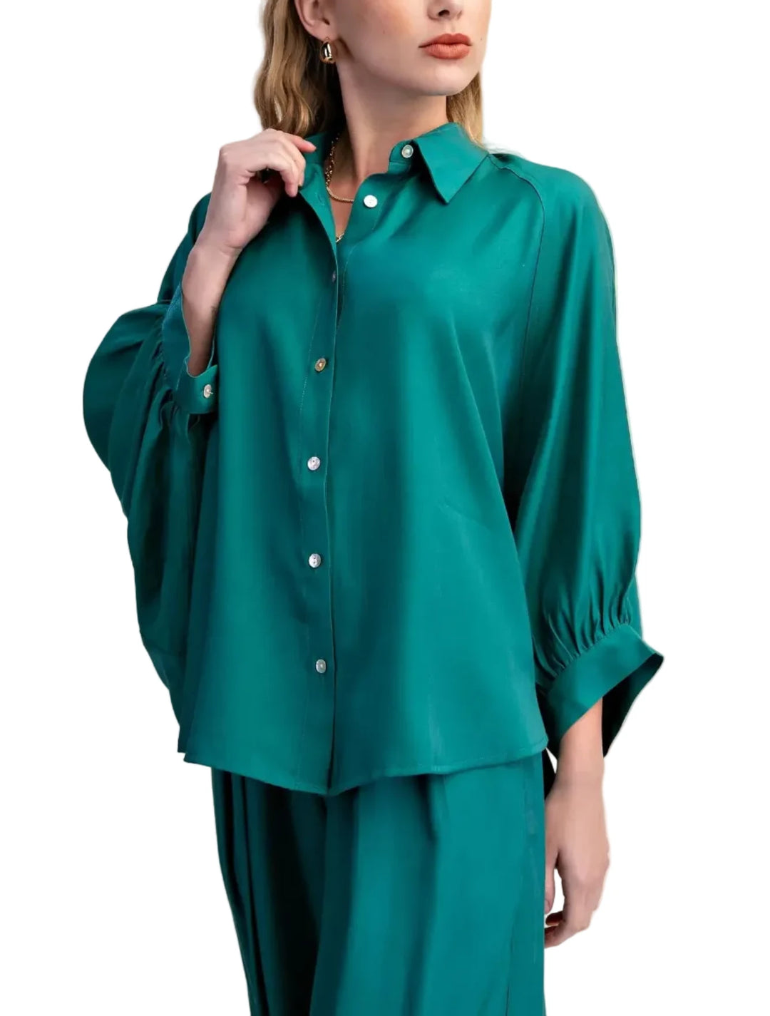 A woman wearing a teal green satin-like button-up blouse with voluminous three-quarter sleeves and matching trousers, posed against a solid beige studio background.