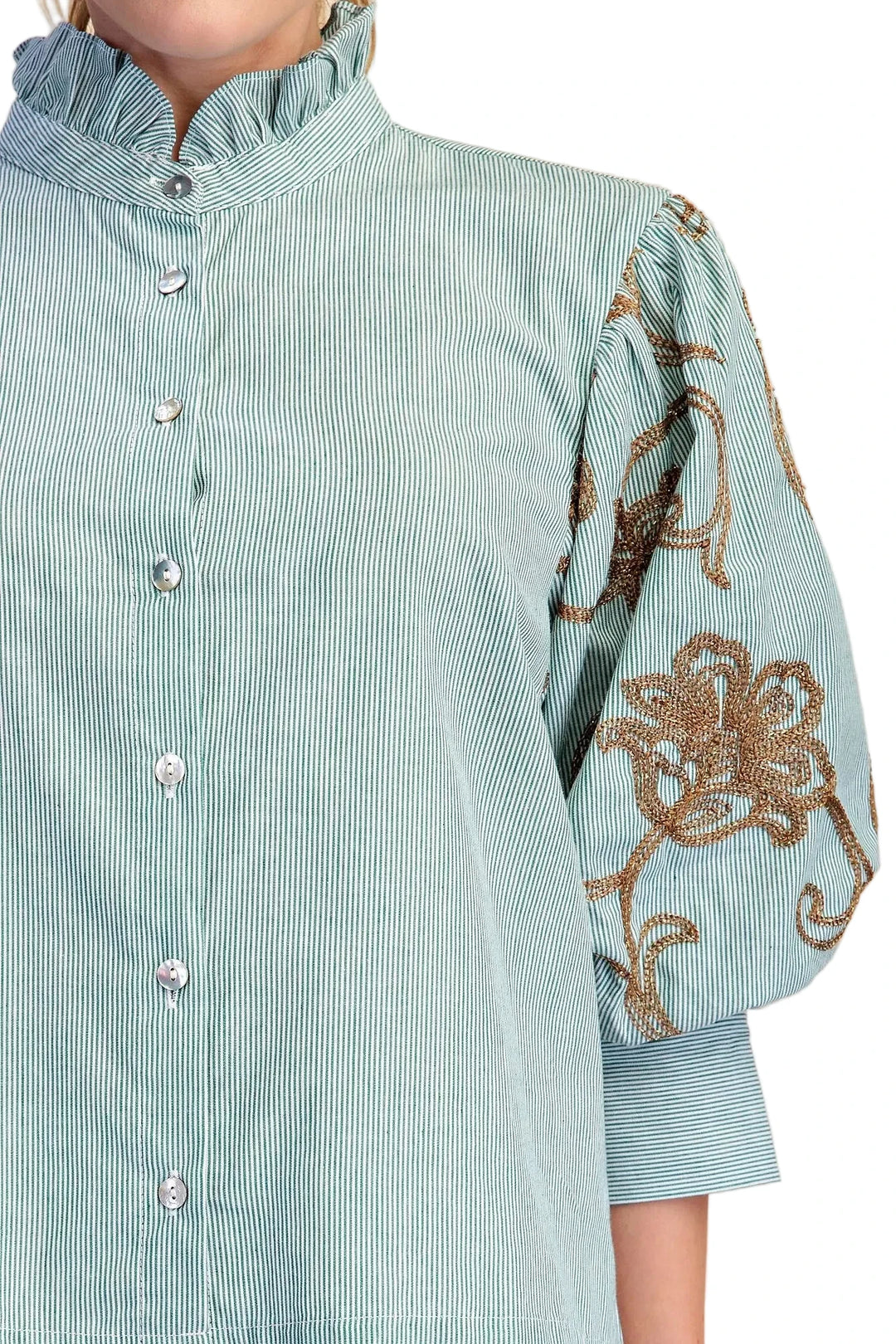 A close-up of a light blue and white striped blouse with a ruffled mock neck, button front, and voluminous sleeves featuring brown floral embroidery.