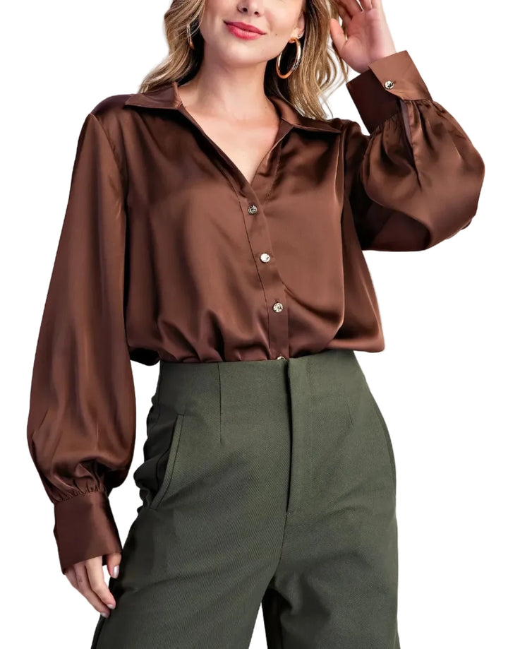 A woman modeling a brown satin long-sleeve button-up blouse with gathered cuffs, paired with olive green trousers, against a light gray studio background.