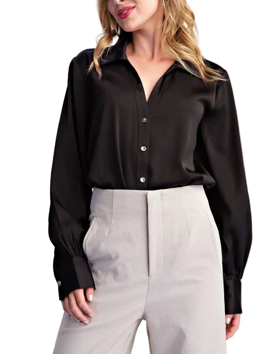 A woman wearing a black long-sleeve button-up blouse tucked into light gray high-waisted trousers, photographed against a plain light beige studio background.