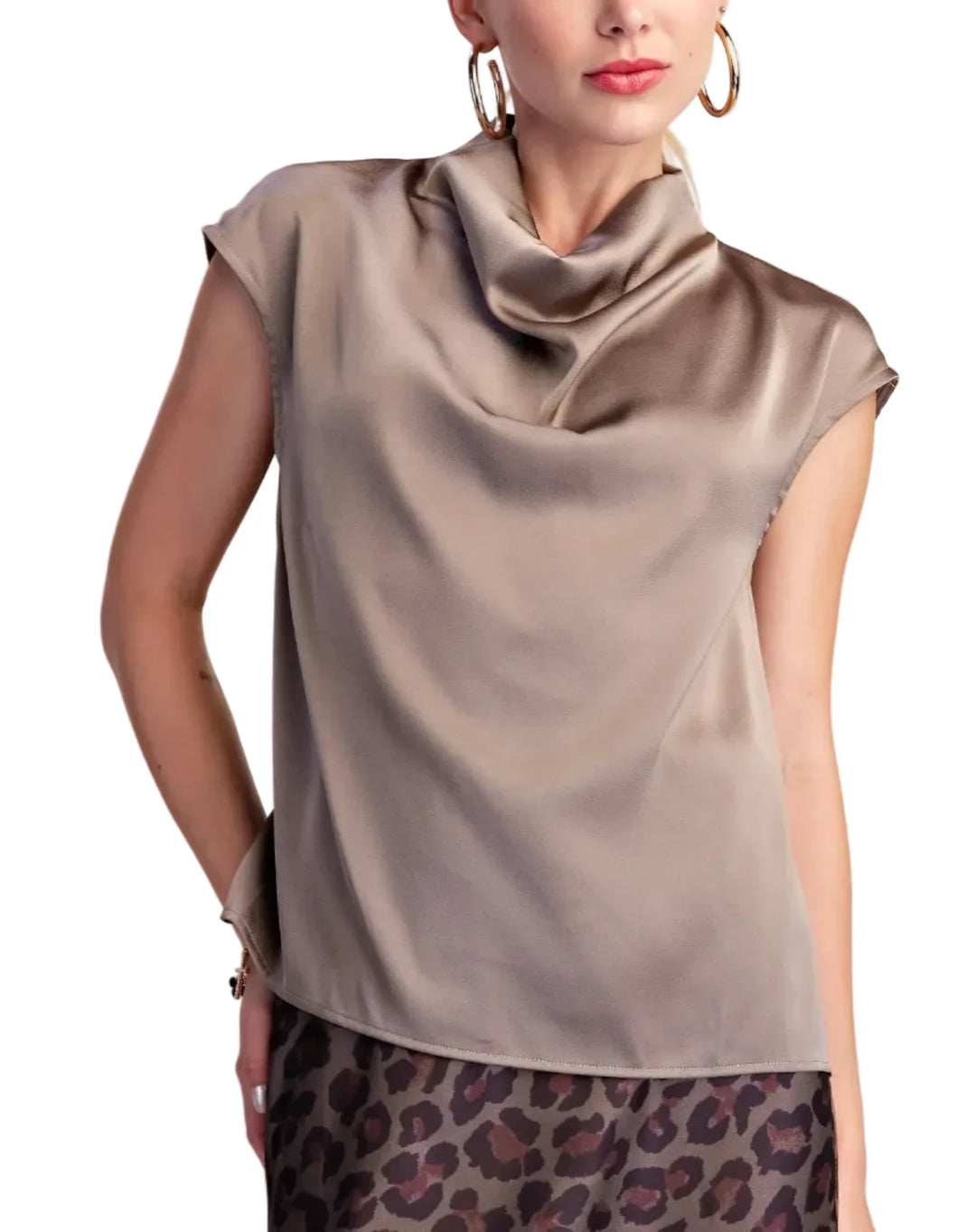 A woman wearing a taupe satin-like cowl-neck top with cap sleeves and a leopard-print skirt, photographed against a plain light beige studio background.