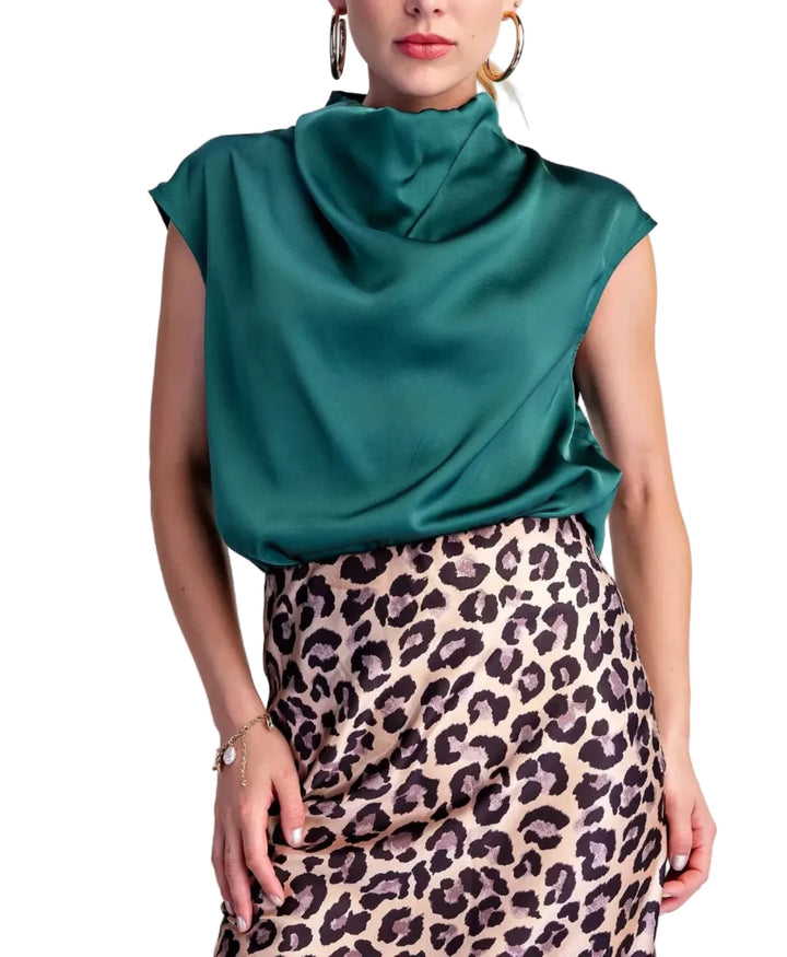 A woman modeling a satin-like teal cowl-neck top paired with a leopard-print skirt, against a plain light beige studio background.