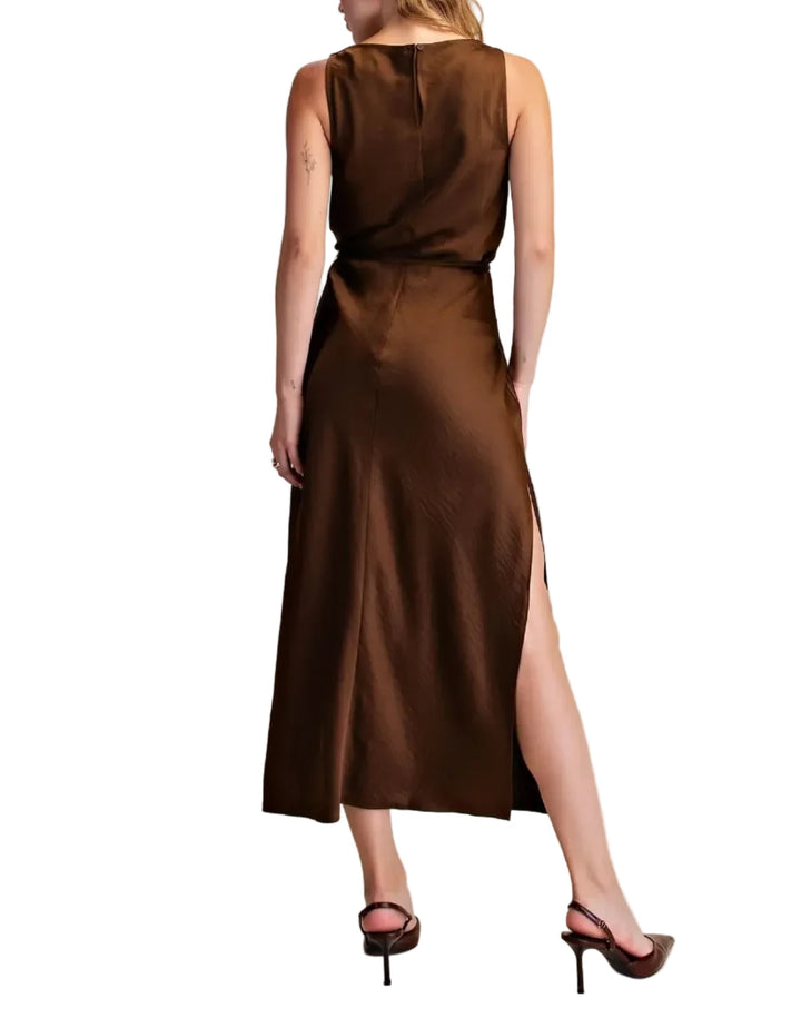 A woman wearing a sleeveless brown midi dress with a high side slit, shown from the back against a plain beige studio background.