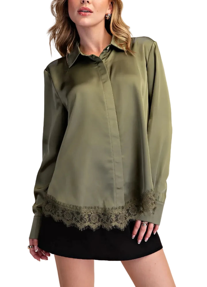 A woman wearing an olive green satin button-up blouse with a lace hem detail, paired with a black skirt, against a solid beige background.
