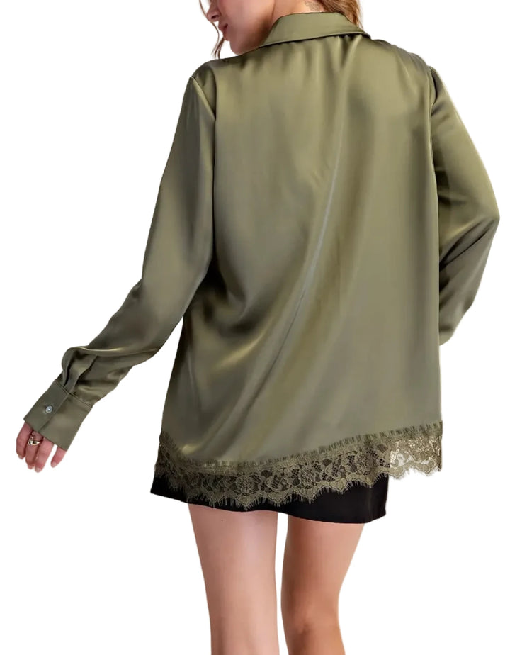A woman shown from the back wearing an oversized olive green satin shirt jacket with a lace hem, paired with a black skirt, against a solid beige background.