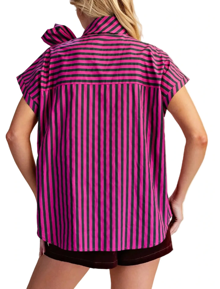 A woman shown from the back wearing a short-sleeve collared blouse with vertical pink and dark stripes and dark shorts, against a plain beige studio background.