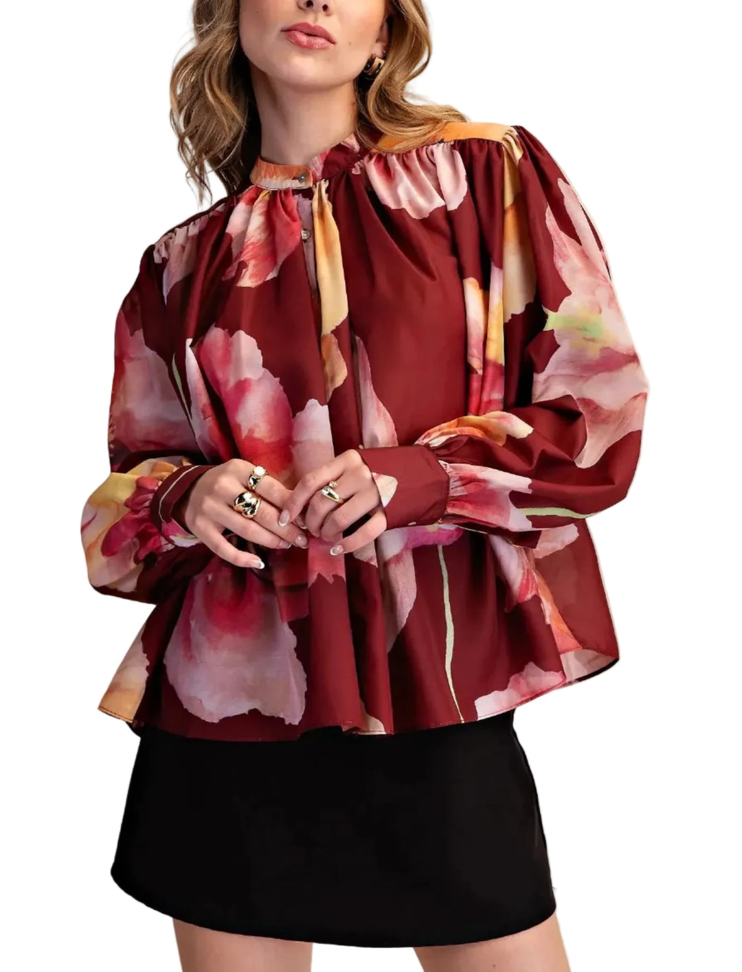 A woman wearing a long-sleeve blouse with a burgundy base and a large pink, red, and yellow floral print, paired with a black skirt, against a solid beige background.