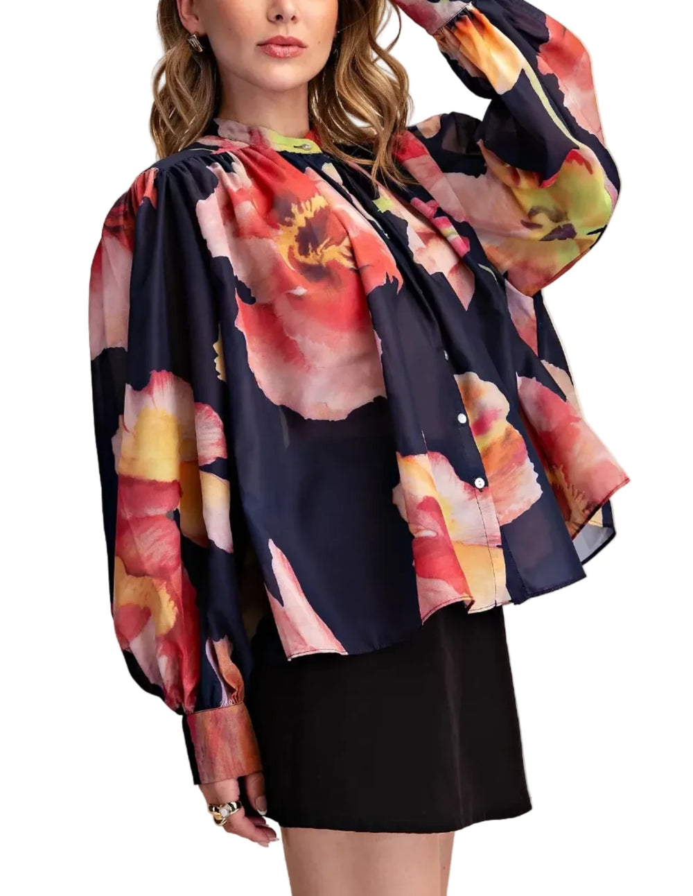 A woman wearing a navy blue long-sleeve blouse with a large, vibrant watercolor floral print in red, pink, orange, and yellow, paired with a black skirt, against a solid beige background.