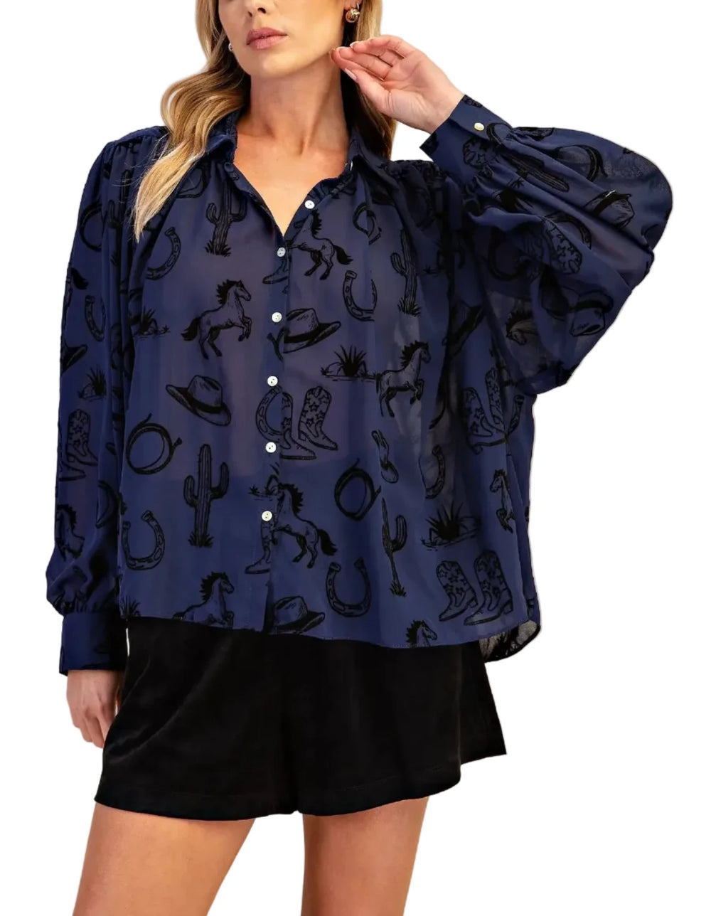 A woman modeling a navy blue long-sleeve button-up blouse with a black western-themed print of cacti, horseshoes, and boots, paired with black shorts against a solid beige background.
