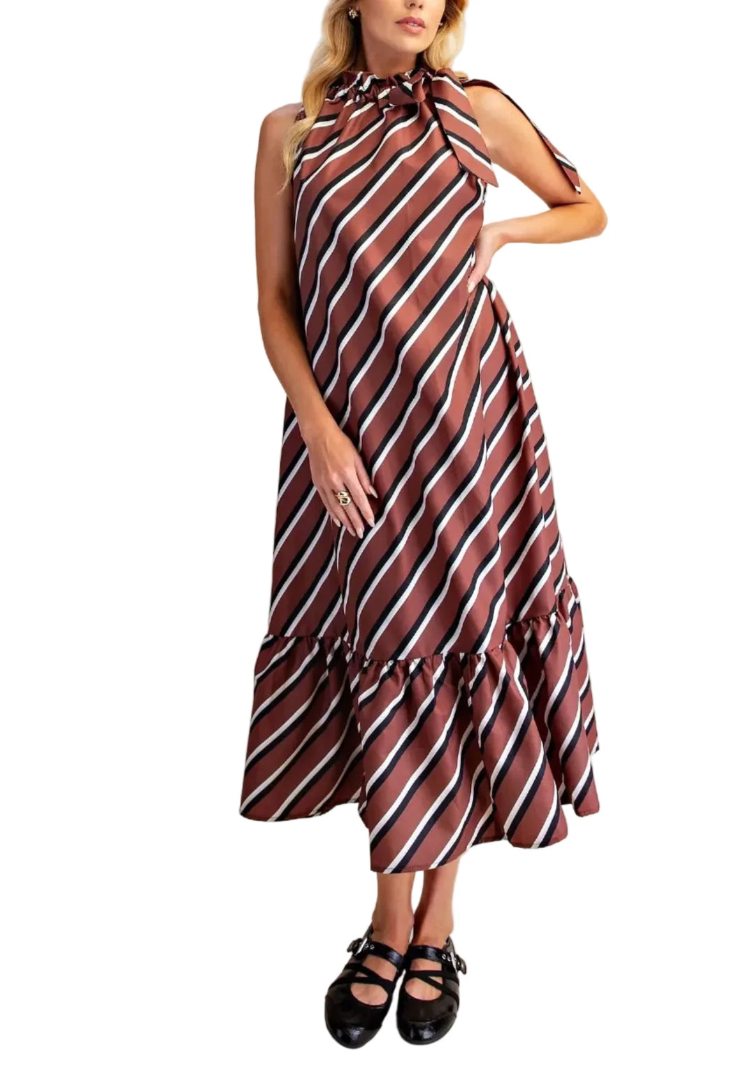 A woman modeling a sleeveless midi dress with diagonal stripes in brown, white, and black, featuring a tie-neck and ruffled hem, paired with black Mary Jane shoes against a solid beige background.