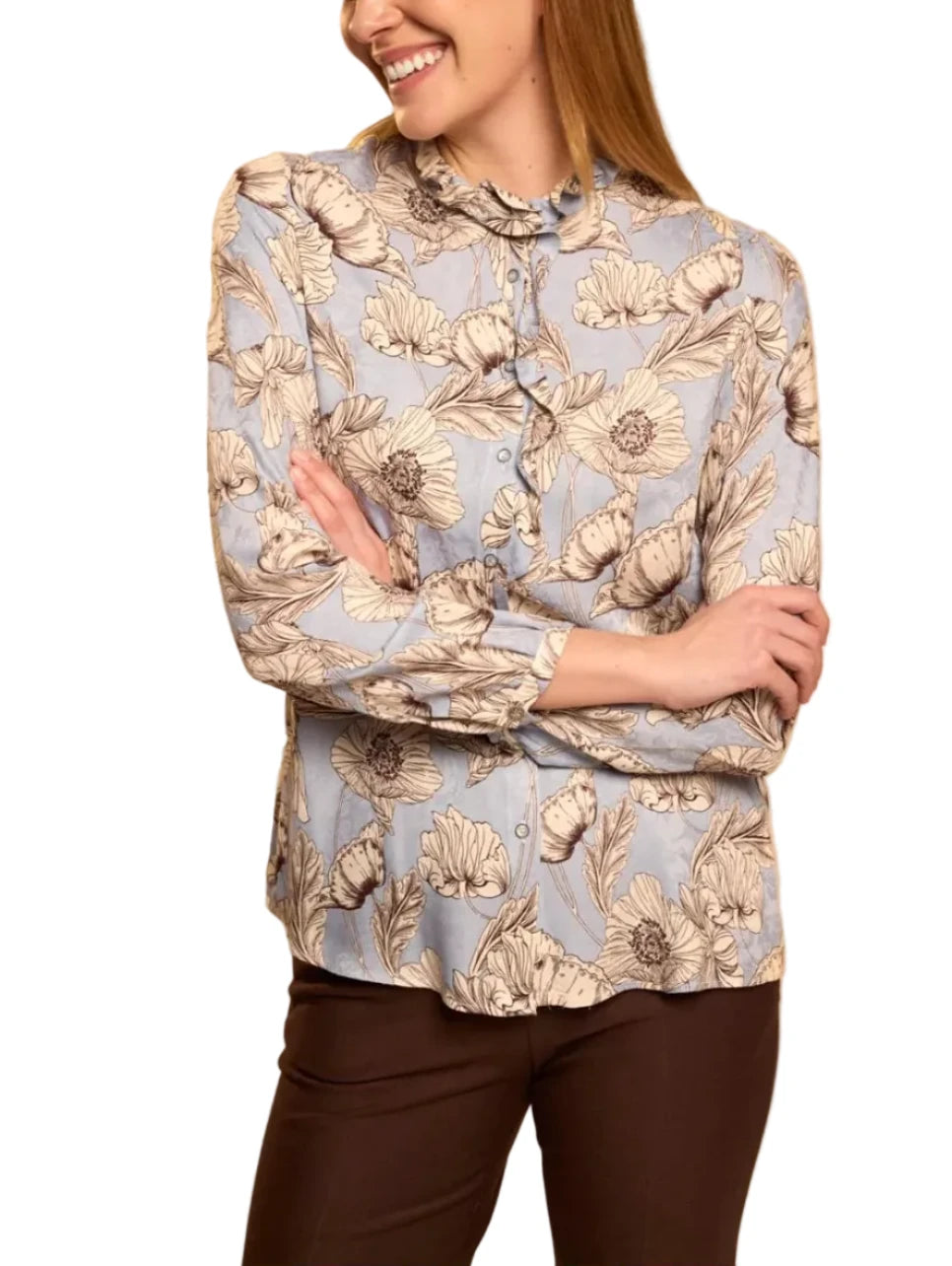 A woman wearing a light blue long-sleeve blouse with a beige and brown floral print, paired with dark brown pants, standing against a solid beige background.