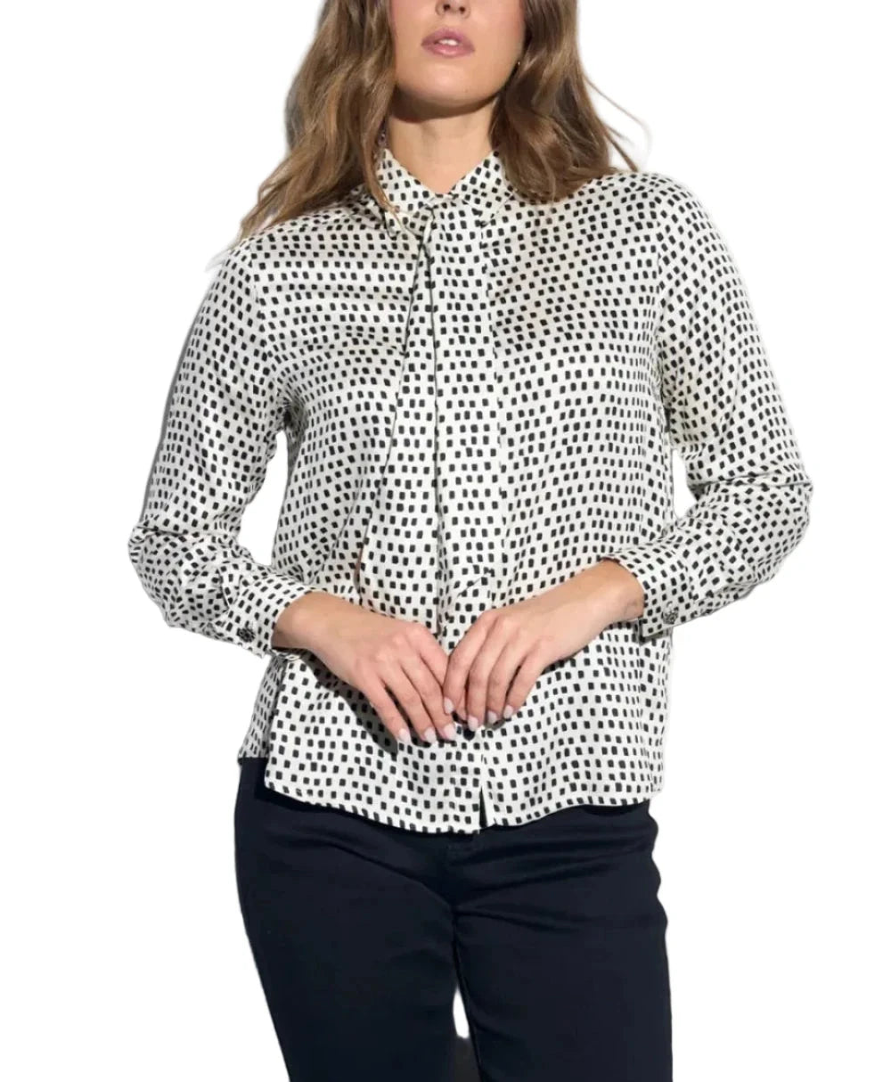 A woman modeling a black and white polka dot button-down shirt with long sleeves, paired with black pants, against a plain white background.
