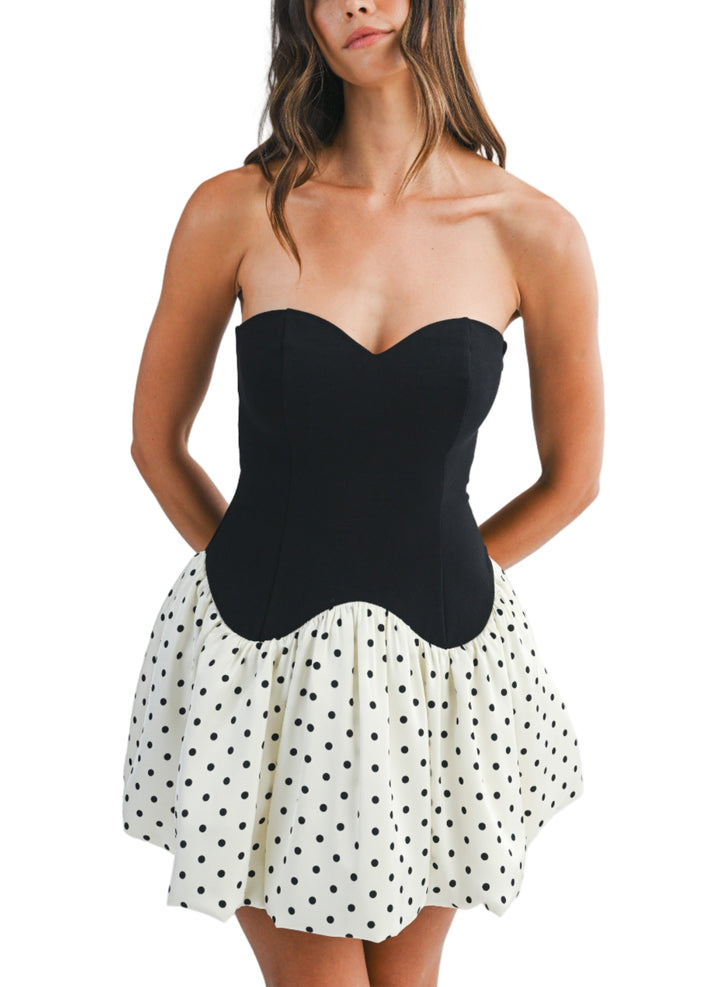 Woman wearing a strapless black top and polka dot skirt on a white background