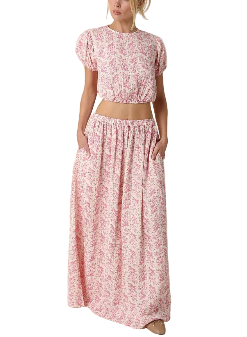 Twirl into spring with this adorable two-piece set featuring a cropped top with charming puff sleeves and an all-over pink floral print. The coordinating maxi skirt completes the look with the same delicate botanical design, creating a perfectly put-together outfit that's effortlessly chic. Whether you're heading to brunch or a garden party, this set brings feminine flair and fun to any occasion.