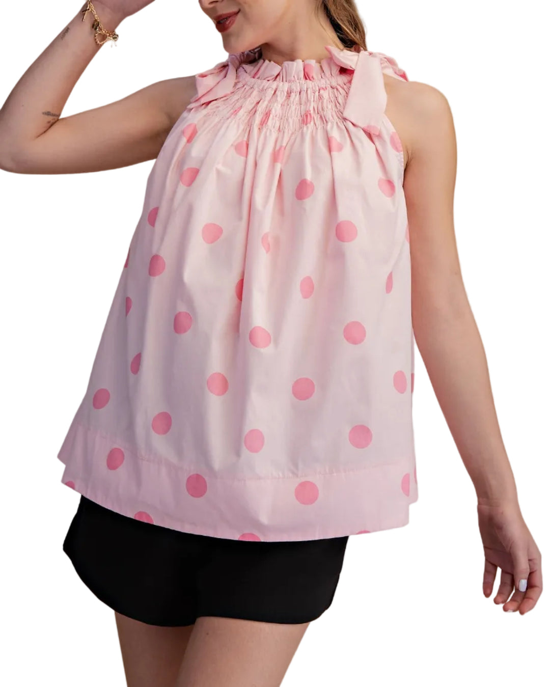 Woman wearing a pink polka dot top and black shorts on a beige background