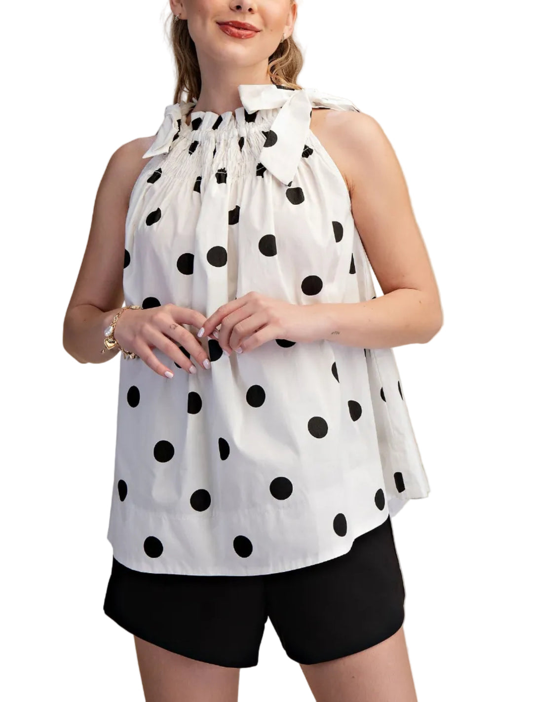 Woman wearing a white sleeveless top with black polka dots and black shorts on a beige background