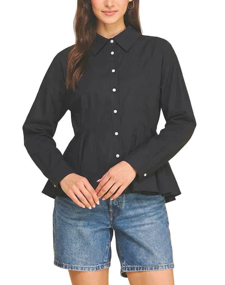 A woman modeling a black long-sleeve button-up blouse with a pointed collar and peplum hem, paired with blue denim shorts, against a solid beige background.