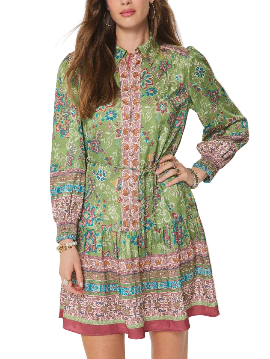 A woman modeling a long-sleeve, collared mini dress with a green base and a colorful bohemian-style floral and geometric print. The dress features a tie waist and a tiered skirt, shown against a plain light gray studio background.