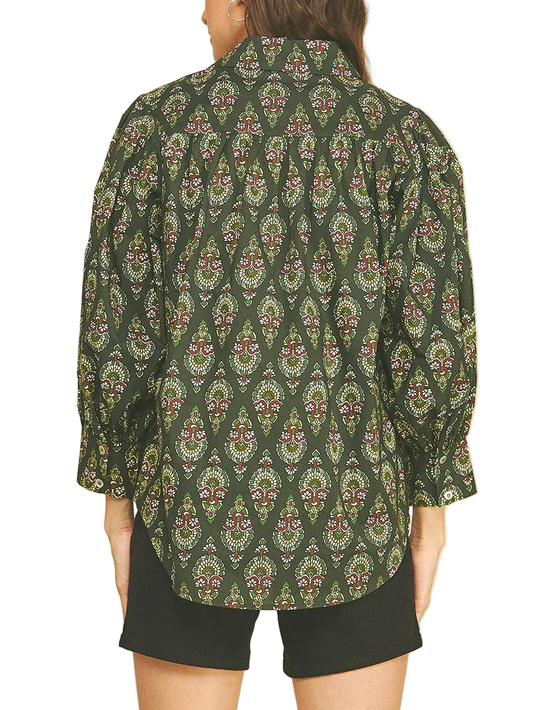 A woman shown from the back wearing a dark green long-sleeve button-up shirt with a detailed multicolor paisley and floral pattern, paired with black shorts, against a solid beige background.