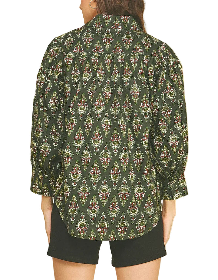A woman shown from the back wearing a dark green long-sleeve button-up shirt with a detailed multicolor paisley and floral pattern, paired with black shorts, against a solid beige background.