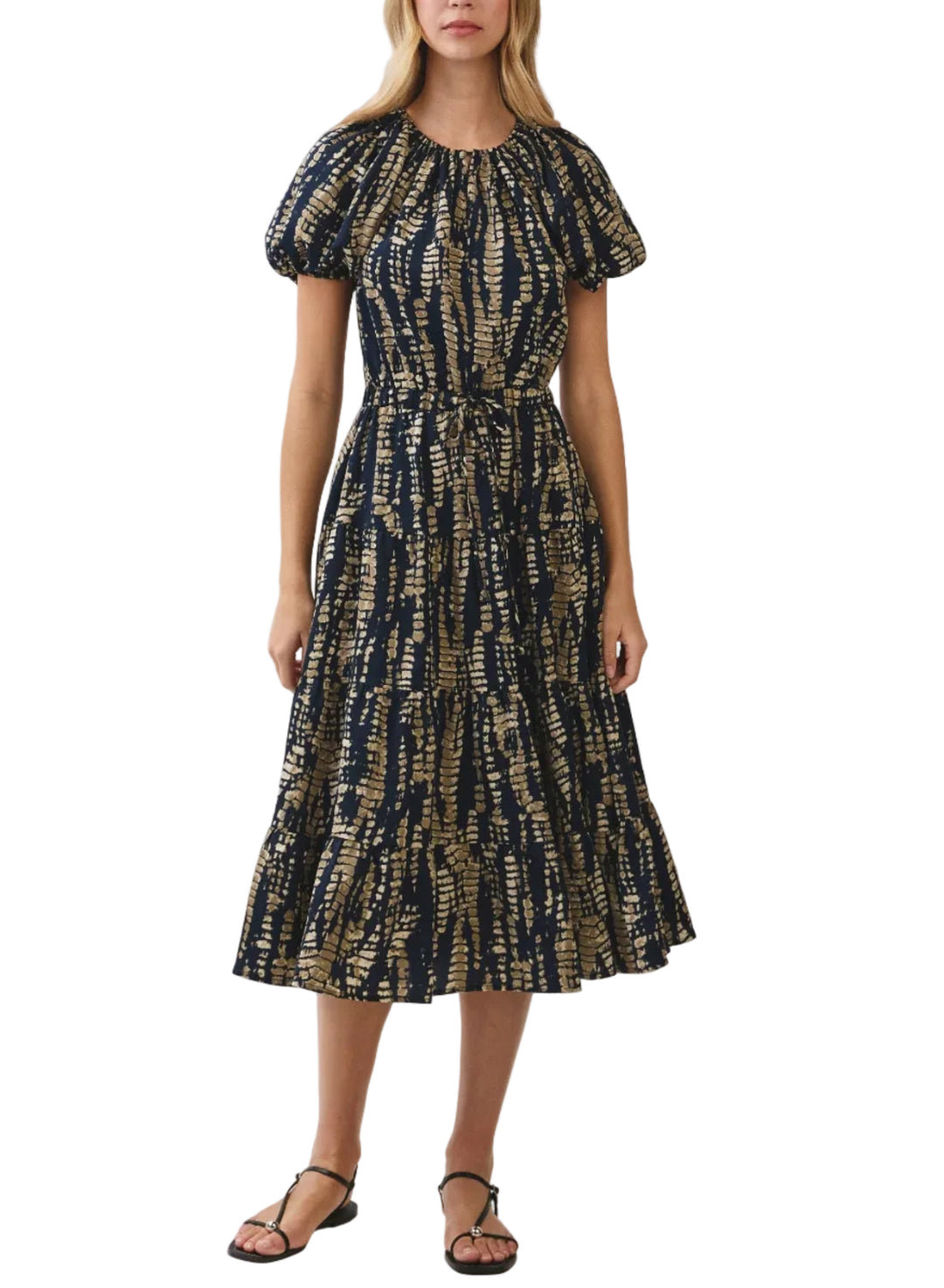 A woman modeling a short-sleeved midi dress with a dark navy blue and beige abstract pattern, standing against a light gray studio background.