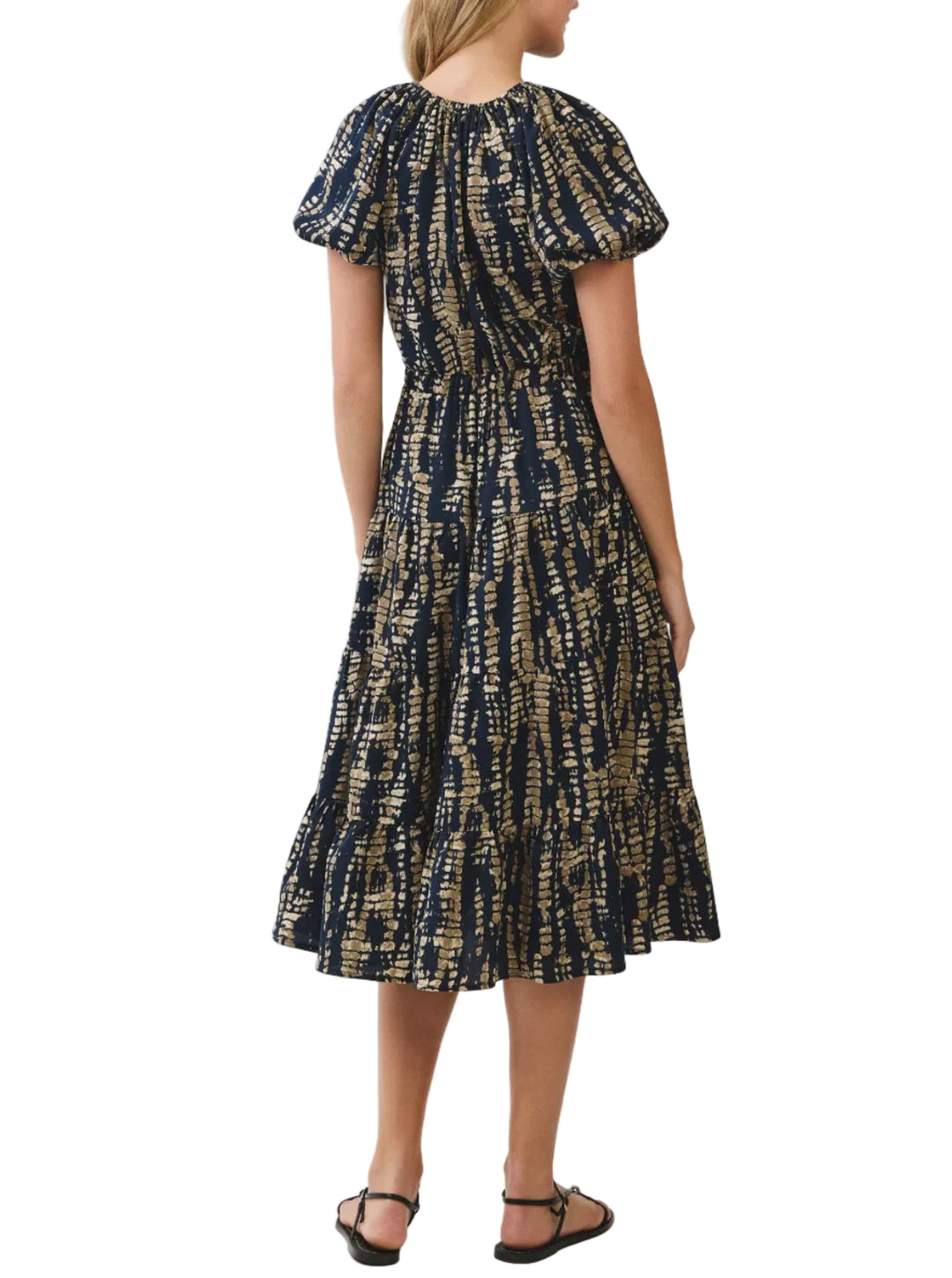 A woman wearing a short puff-sleeve midi dress with a navy blue and beige abstract tie-dye pattern, shown from the back against a light gray studio background.