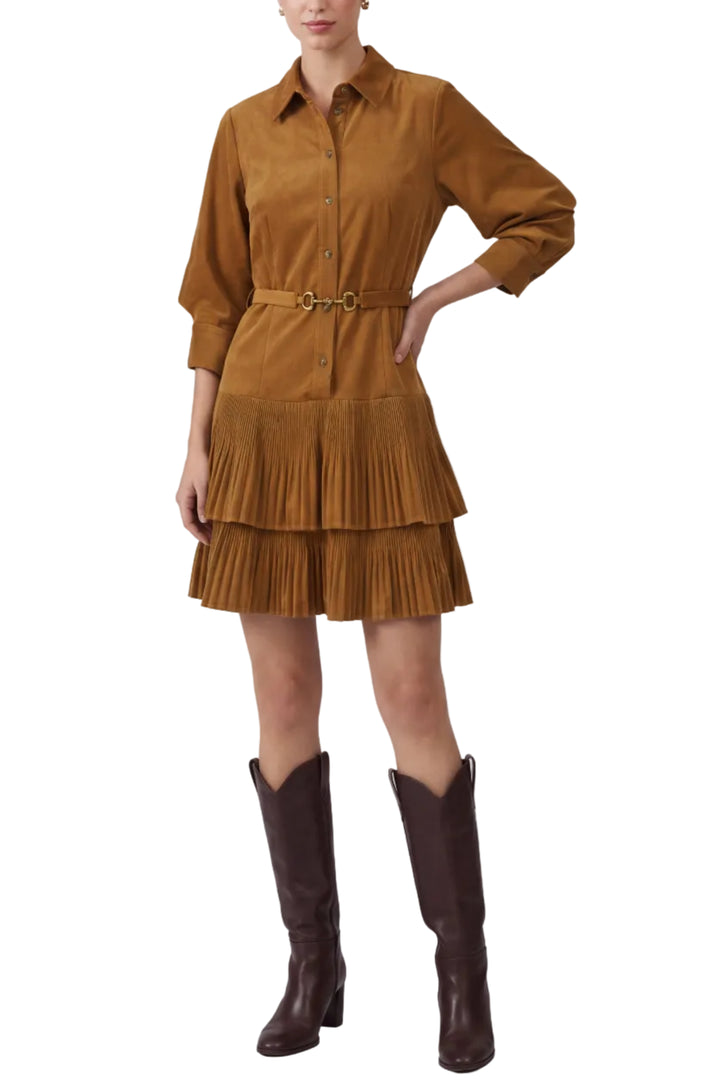 A woman modeling a mustard brown corduroy shirt dress with a matching belt and a pleated tiered skirt, paired with dark brown cowboy boots, against a light gray studio background.