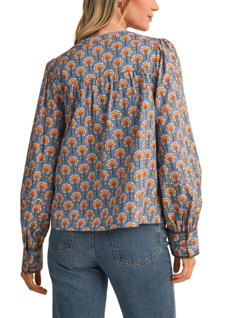 A woman shown from the back wearing a long-sleeve blouse with a blue base and an orange and yellow floral pattern, paired with blue jeans, against a solid beige background.