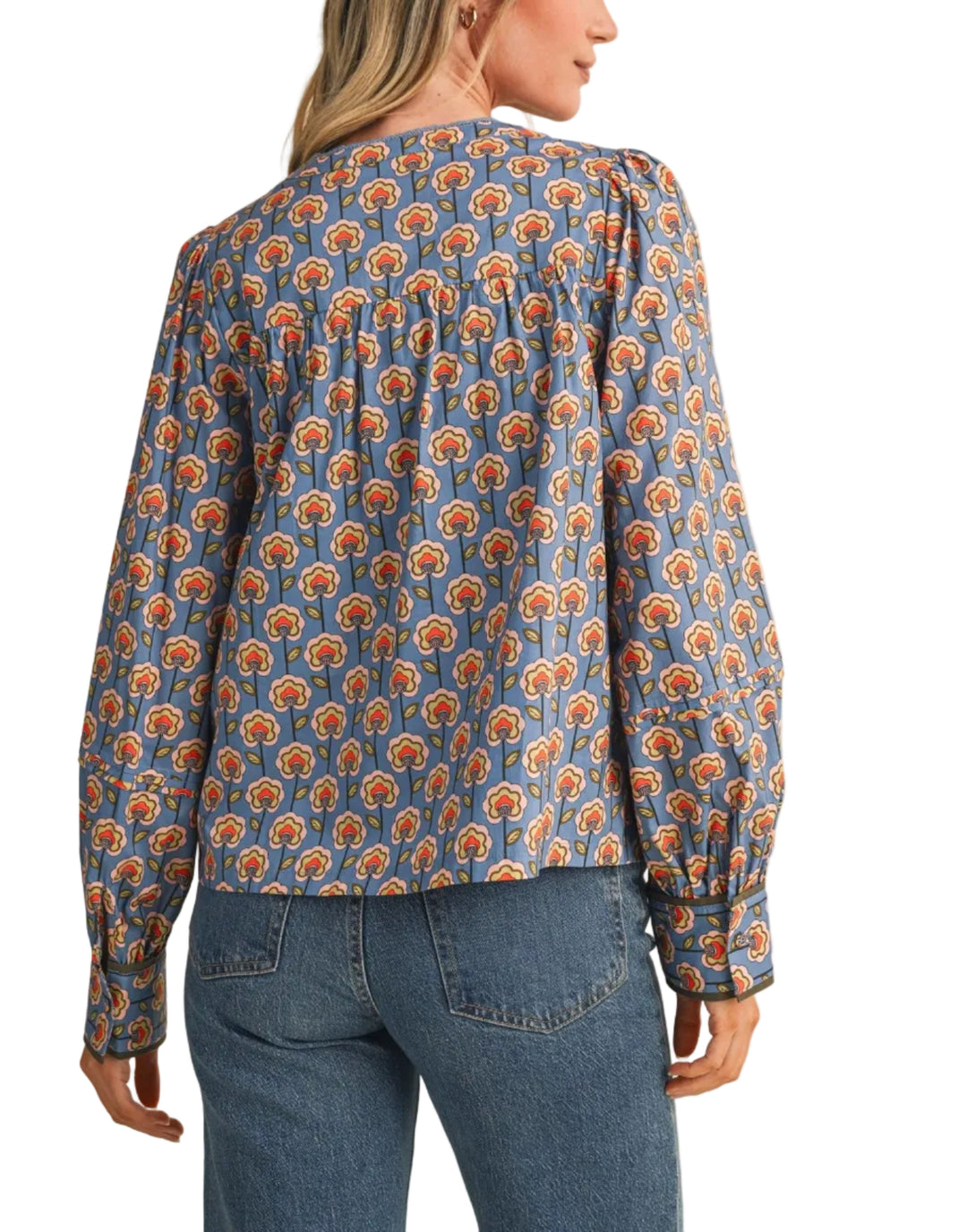 A woman shown from the back wearing a long-sleeve blouse with a blue base and an orange and yellow floral pattern, paired with blue jeans, against a solid beige background.