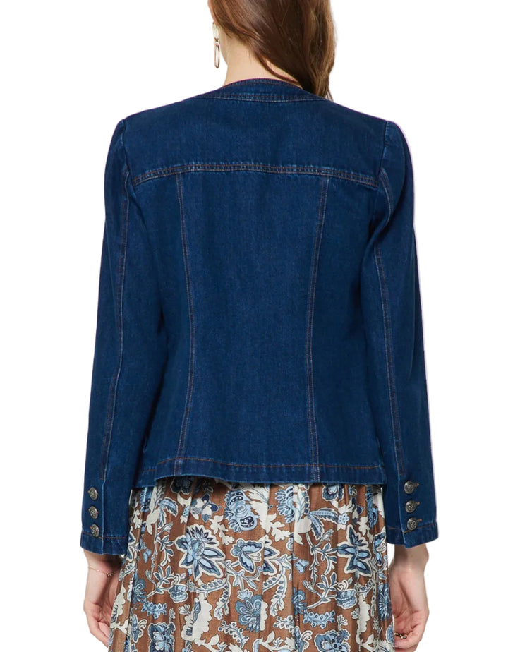 A woman shown from the back wearing a dark blue denim jacket with button details on the cuffs and a brown floral patterned skirt, against a plain light gray background.