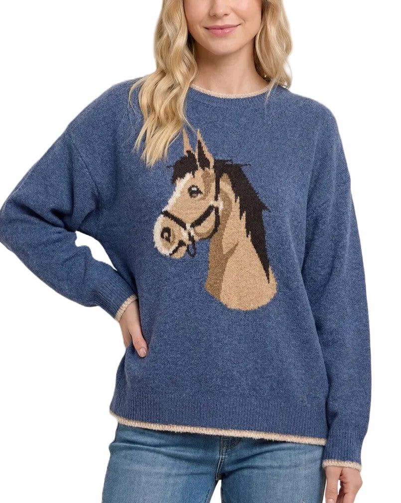 A woman wearing a heathered blue knit sweater with a large horse head graphic on the front, paired with blue jeans, against a solid light beige background.