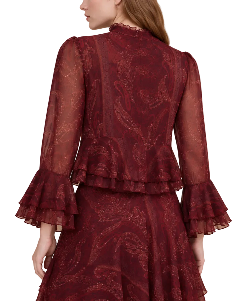 A woman shown from the back wearing a burgundy sheer lace dress with a paisley pattern, ruffled long sleeves, and a high lace collar, set against a solid beige background.