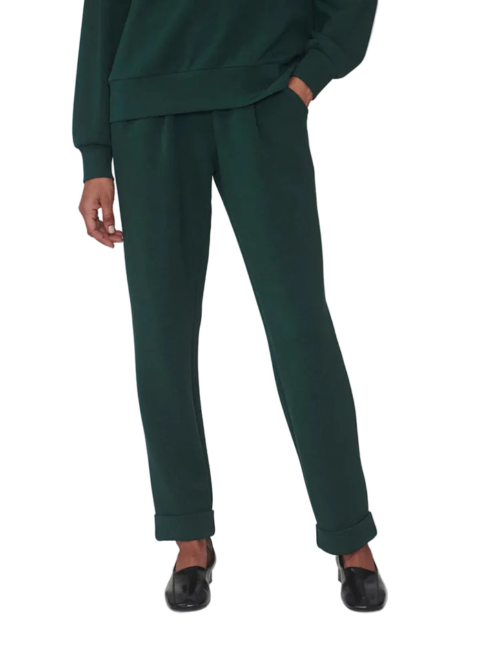 A model wearing dark green cropped sweatpants with a matching sweatshirt and black loafers, shown from the waist down against a light gray studio background.