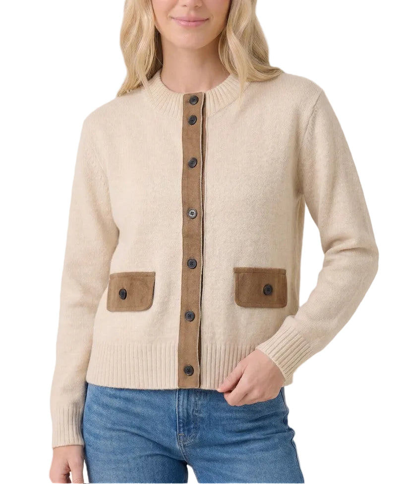 A woman wearing a cream-colored knit cardigan with brown suede-like front placket and pocket details, paired with blue jeans, against a solid light beige background.