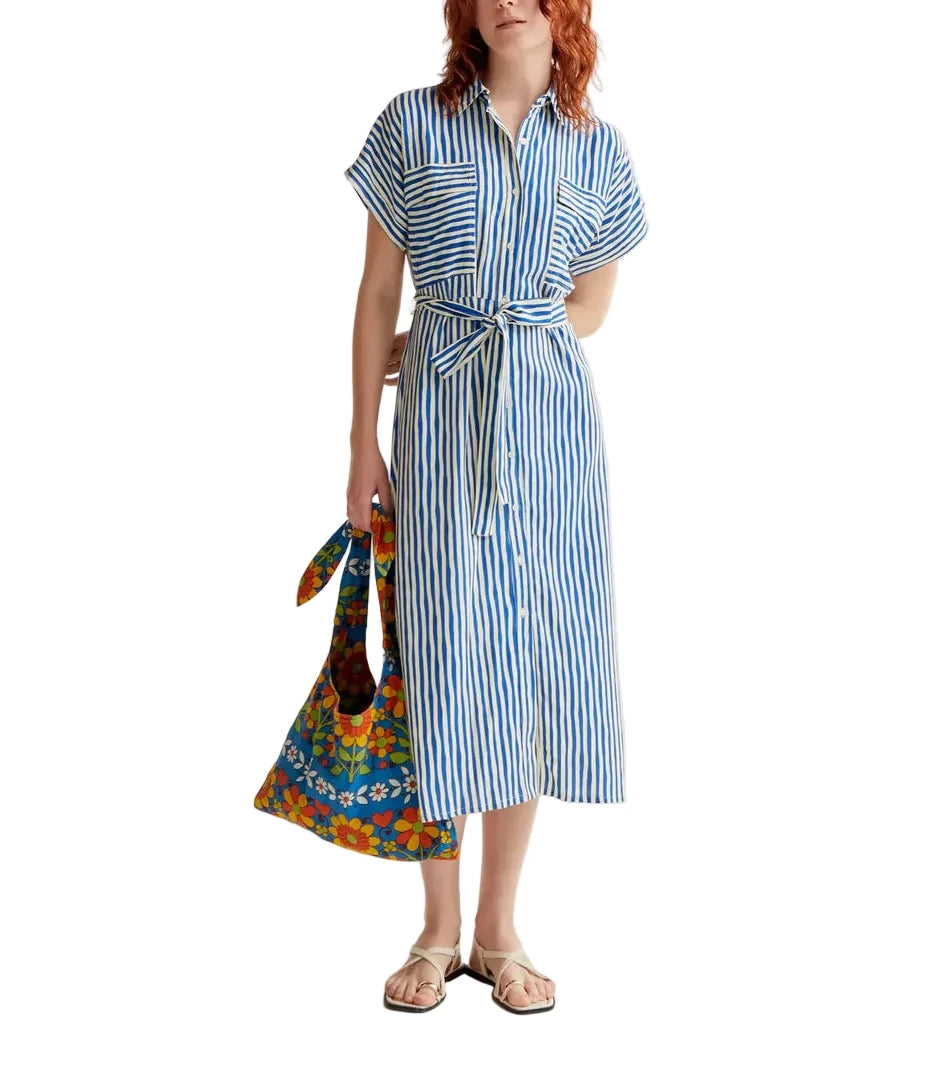 Woman wearing a blue and white striped dress holding a colorful bag on a plain background