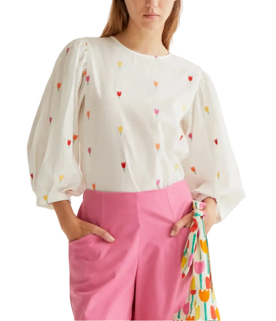 Woman wearing a white blouse with colorful heart patterns and pink pants on a white background
