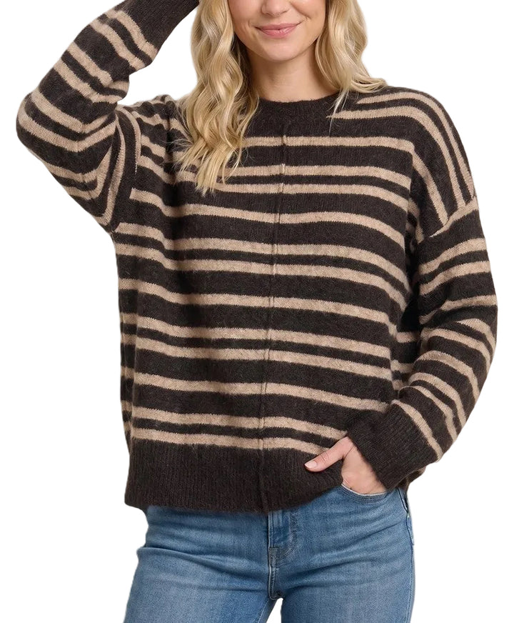 A woman wearing a dark brown and beige horizontally striped knit sweater with blue jeans, posing against a solid light beige background.