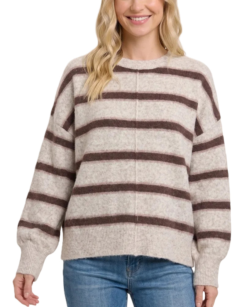 A woman wearing a cream and dark brown horizontally striped knit sweater with blue jeans, photographed against a solid light beige background.