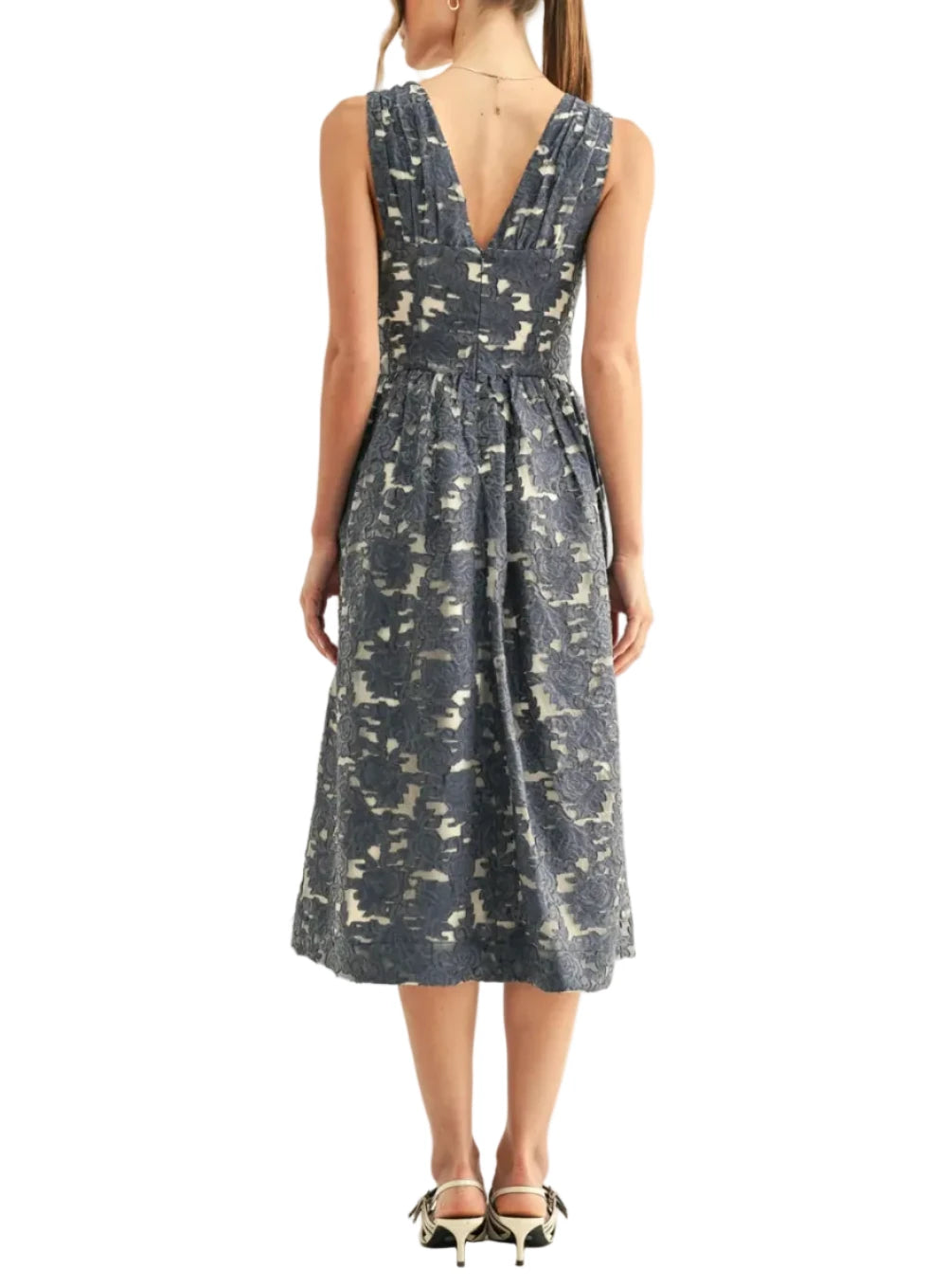 Cut from an intricate jacquard fabric in a denim blue jacquard colorway, it features a detailed floral pattern woven over a lighter, semi-sheer backing to create beautiful visual depth. The sleeveless bodice is designed with a deep V-neckline, gathered supportive cups, and a delicate tie detail at the center of the bust. Below the bust, a structured, corset-style waistband cinches the frame before flaring out into a voluminous, subtly pleated A-line midi dress
