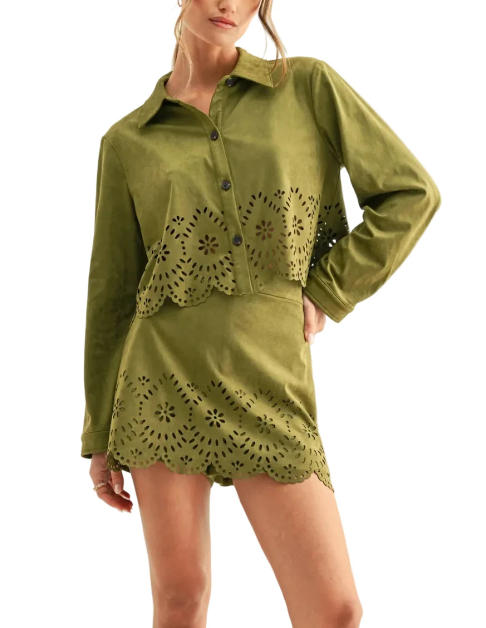 A woman modeling a long-sleeve olive green shirt dress with laser-cut eyelet floral patterns along the front and hem, set against a plain off-white studio background.