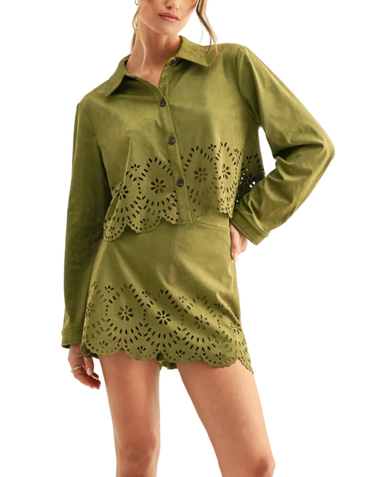 A woman modeling a long-sleeve olive green shirt dress with laser-cut eyelet floral patterns along the front and hem, set against a plain off-white studio background.