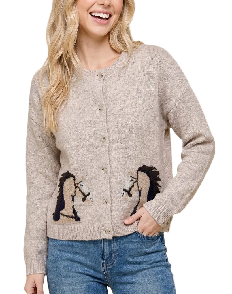 A woman wearing a light beige button-up cardigan sweater with embroidered horse designs on the lower front, paired with blue jeans, against a solid light beige background.
