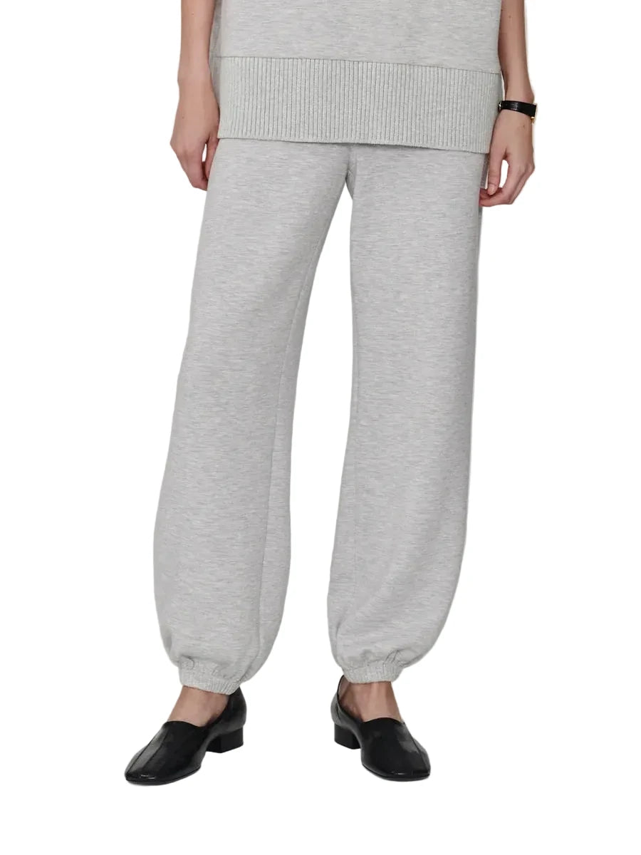 A model from the waist down wearing light heather gray wide-leg sweatpants with elastic cuffs, paired with black loafers, against a plain light gray studio background.
