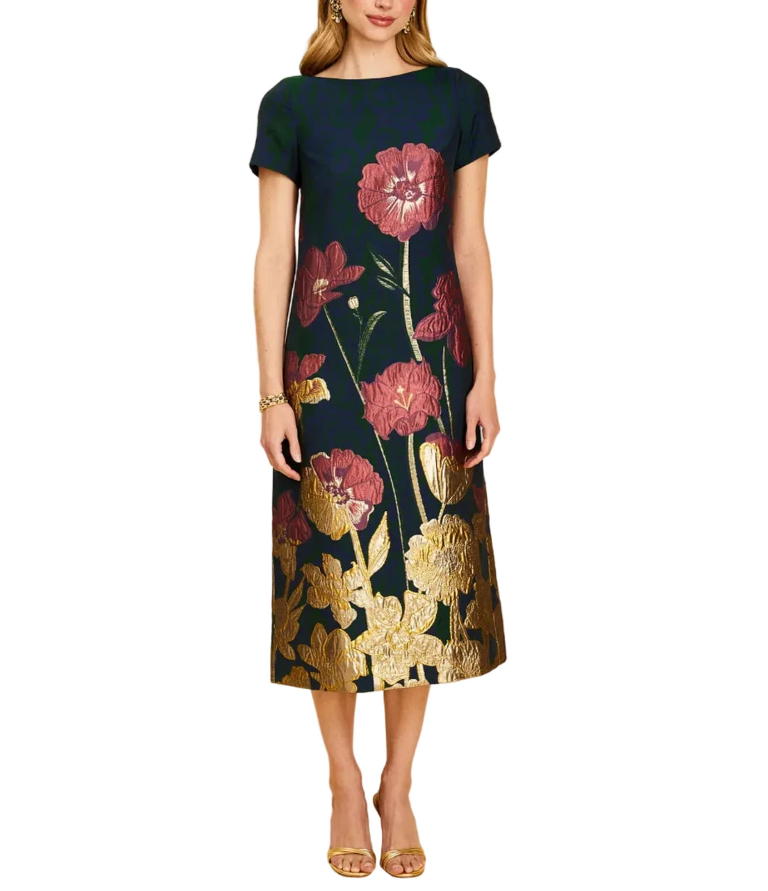 A woman modeling a short-sleeve midi dress with a dark navy base and a large floral print in dusty pink and metallic gold, set against a solid beige studio background.